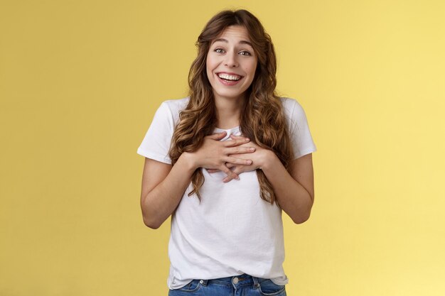 Sorprendido tocado agradecido encantadora mujer caucásica de pelo rizado apreciar esfuerzo agradeciendo increíble regalo presionar manos corazón movido encantador bonito presente sonriendo ampliamente agradecido fondo amarillo