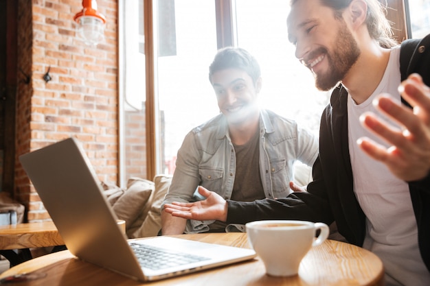 Sorprendidos amigos sonrientes con laptop en café