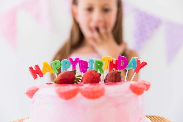 Sorpresa linda chica detrás de delicioso pastel de cumpleaños de fresa