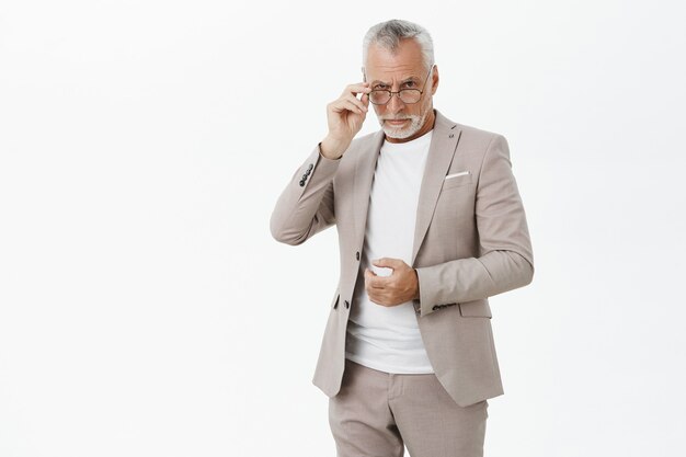 Sospechoso anciano de aspecto serio en traje mirando por encima de las gafas escéptico