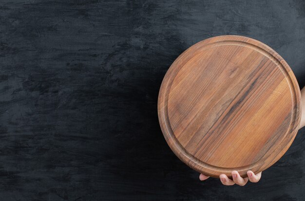 Sosteniendo una bandeja de madera en la mano sobre fondo negro