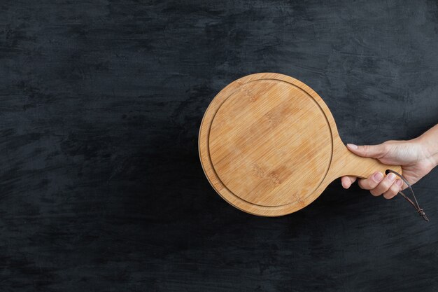 Sosteniendo una bandeja de madera en la mano sobre fondo negro