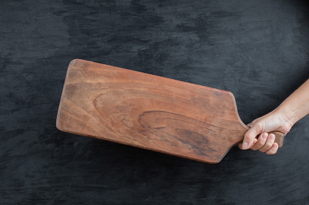 Sosteniendo una bandeja de madera en la mano sobre fondo negro