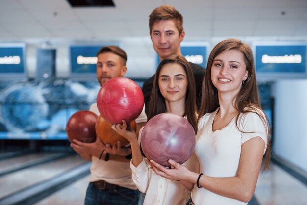 Sosteniendo bolas en las manos. Jóvenes amigos alegres se divierten en el club de bolos en sus fines de semana