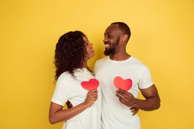 Sosteniendo corazones rojos. Celebración del día de San Valentín, feliz pareja afroamericana aislada sobre fondo amarillo de estudio. Concepto de emociones humanas, expresión facial, amor, relaciones, vacaciones románticas.