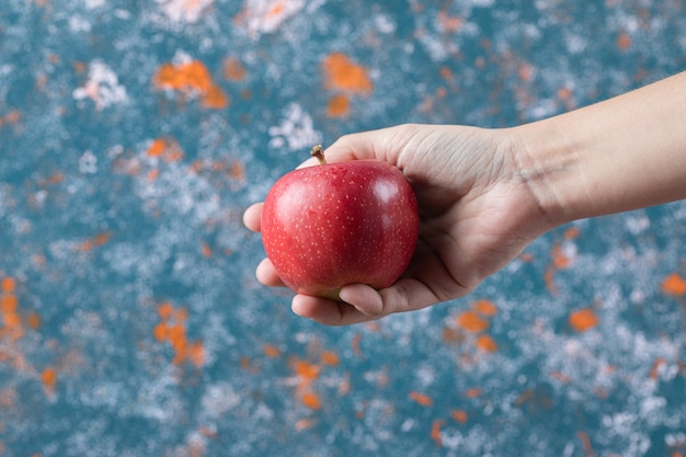 Sosteniendo una manzana roja en la mano sobre la superficie azul