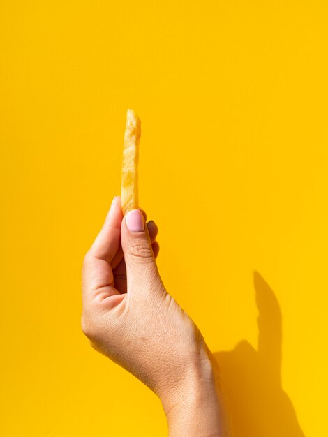 Sosteniendo papas fritas sobre fondo amarillo