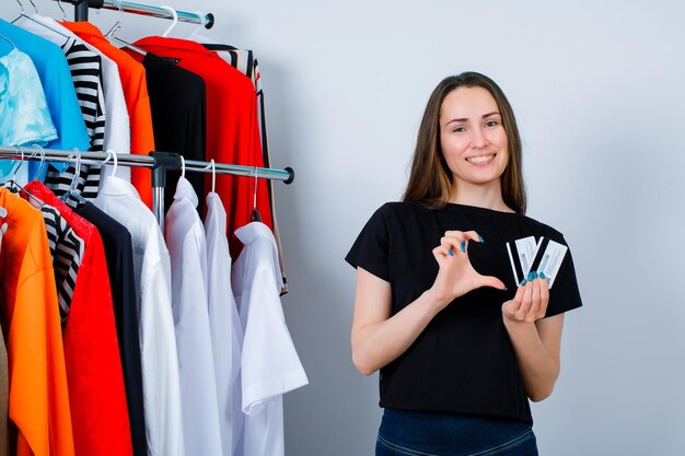 Sosteniendo tarjetas de crédito chica si mostrando gesto de tamaño en el fondo de la ropa