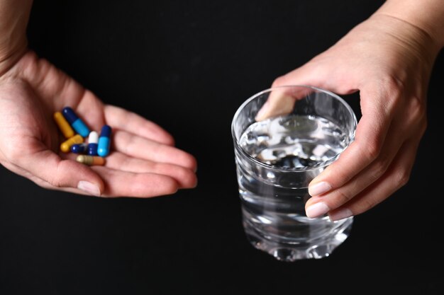 Sosteniendo un vaso de agua y píldoras médicas en las manos.