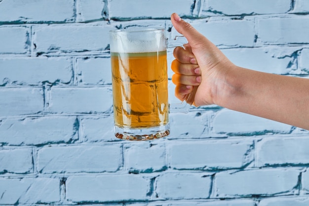 Foto gratuita sosteniendo un vaso de cerveza sobre un fondo azul.