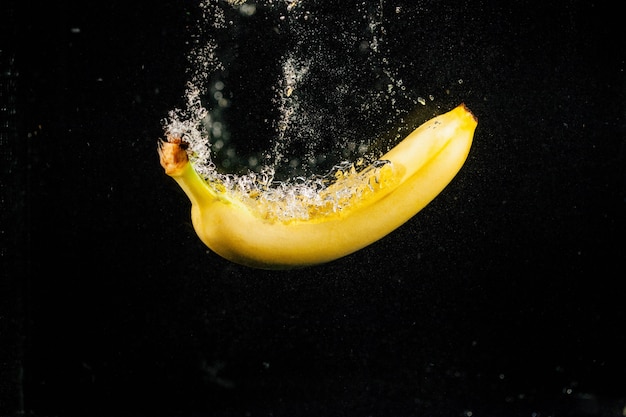 Sprkling plátano amarillo cae en el agua sobre fondo negro