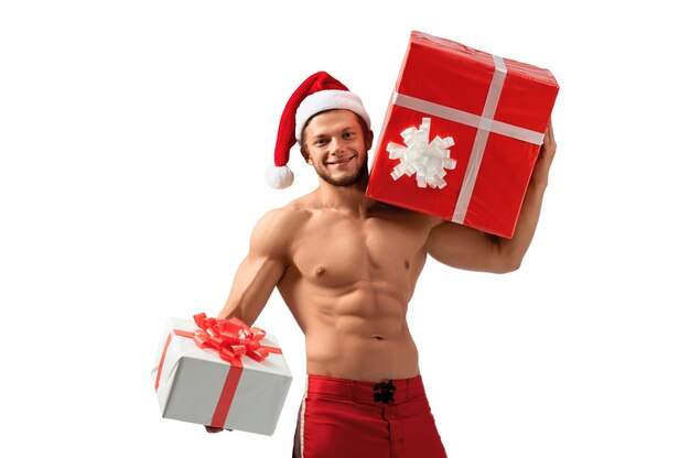 Éste es para ti. Retrato de un hombre rasgado desnudo con sombrero de Santa Claus sosteniendo un regalo y sonriendo ampliamente 2018, 2019.
