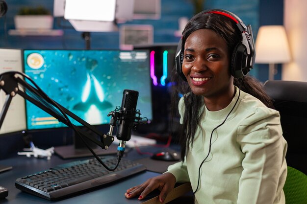 Streamer mujer africana jugador profesional jugando juegos en línea computadora, color rgb. Transmisión de videojuegos virales para divertirse usando auriculares y teclado para el campeonato en línea.