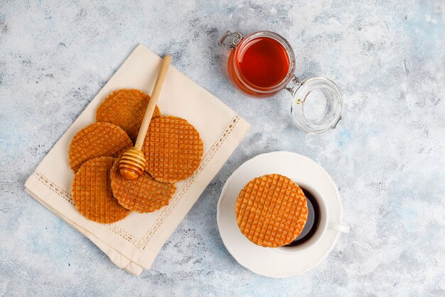 Stroopwafels, gofres holandeses de caramelo con té o café y miel sobre hormigón