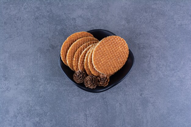 Stroopwafels con piñas aisladas en una placa negra sobre una piedra.