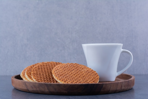 Stroopwafels con una taza de té blanco aislado en una placa de madera sobre una superficie de piedra