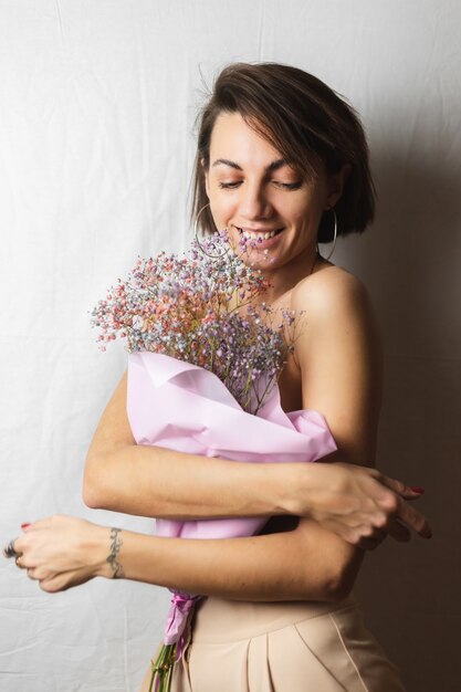 Suave retrato de una mujer joven en un trapo blanco en topless sosteniendo un ramo de flores secas multicolores y sonriendo lindo, anticipación de la primavera