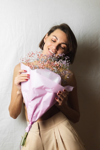 Suave retrato de una mujer joven en un trapo blanco en topless sosteniendo un ramo de flores secas multicolores y sonriendo lindo, anticipación de la primavera