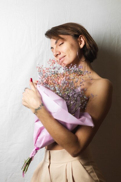 Suave retrato de una mujer joven en un trapo blanco en topless sosteniendo un ramo de flores secas multicolores y sonriendo lindo, anticipación de la primavera