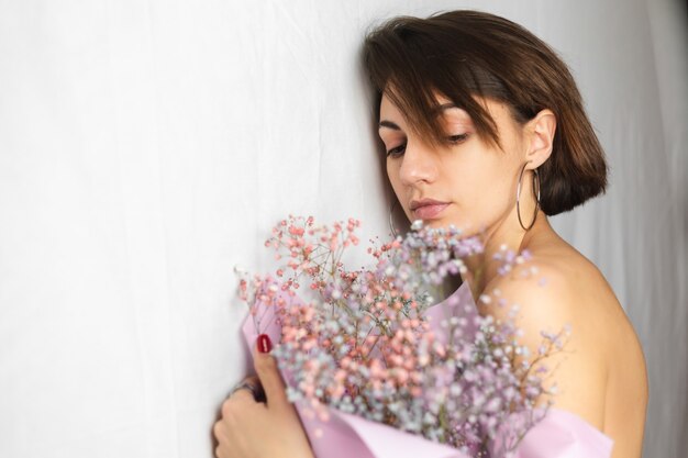 Suave retrato de una mujer joven en un trapo blanco en topless sosteniendo un ramo de flores secas multicolores y sonriendo lindo, anticipación de la primavera