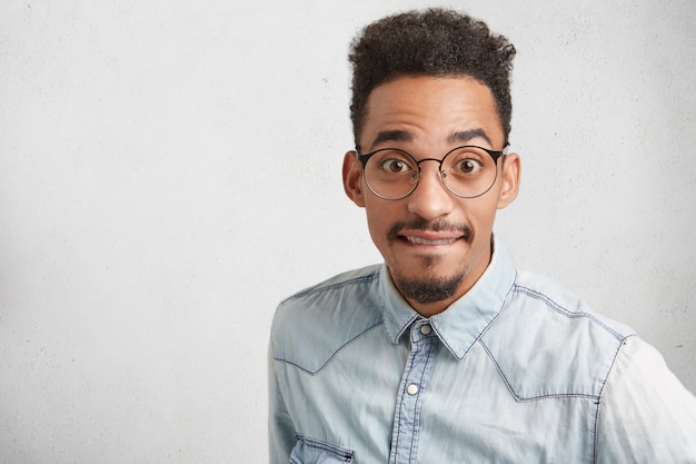 Sudio shot de sorprendido apuesto estudiante con bigote, viste gafas redondas y ropa formal