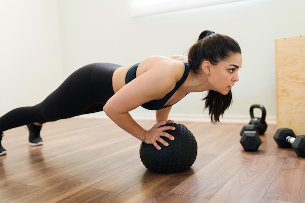 Sudoración con un entrenamiento interválico de alta intensidad. Mujer deportiva caucásica haciendo flexiones con una pelota médica durante su entrenamiento funcional en casa