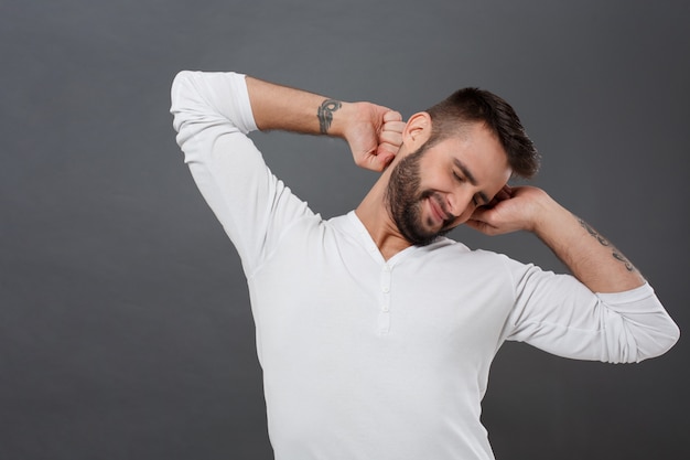 Sueño joven sonriendo, estirando después de despertarse sobre la pared gris