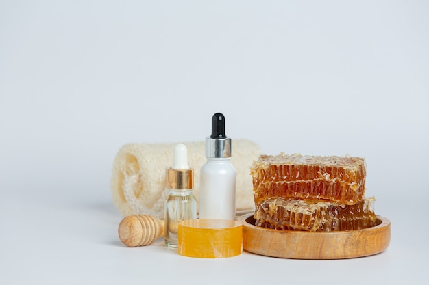 Suero y jabón natural para el cuidado de la piel con miel y panal sobre una superficie blanca.