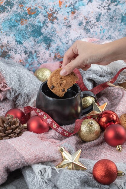 Sumergir la galleta de jengibre en la bebida sobre la mesa cubierta con adornos navideños