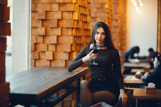 Sumiller degustación de vino tinto. Retrato de mujer elegante con labios rojos de cerca. Señora sosteniendo el vaso con vino tinto y mirando a cámara.