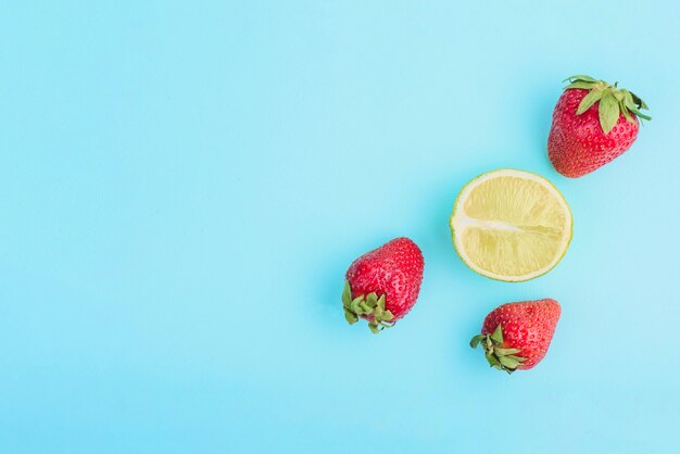 Superficie azul con tres fresas y medio limón