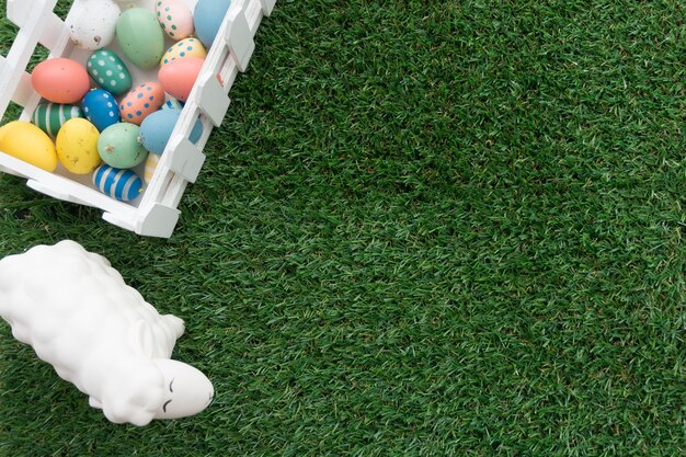 Superficie de hierba con huevos de colores y oveja para el día de pascua