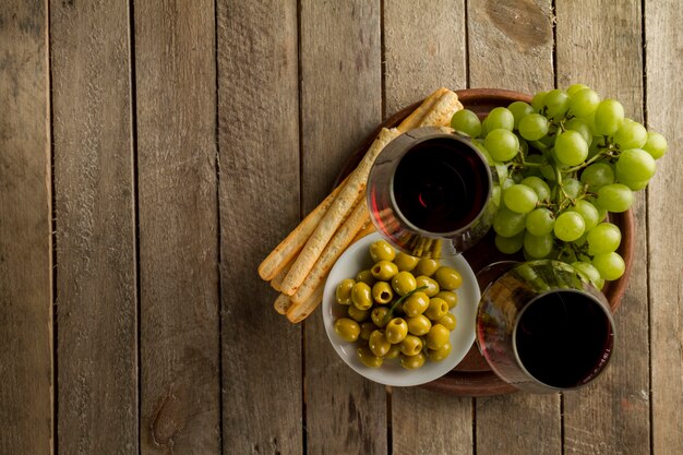 Superficie de madera con aceitunas, uvas y vasos de vino