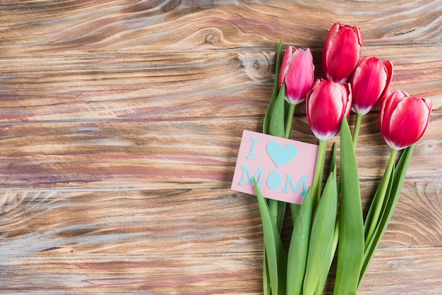 Superficie de madera con flores bonitas y tarjeta para el día de la madre