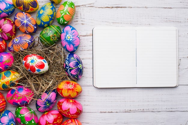 Superficie de madera con huevos de pascua y cuaderno en blanco