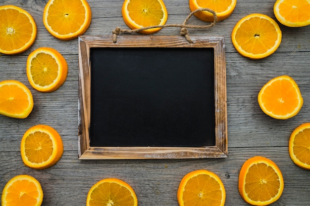 Superficie de madera con pizarra en blanco y rodajas de naranja