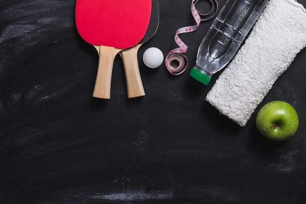 Foto gratuita superficie oscura con raquetas de ping pong, botella de agua y manzana