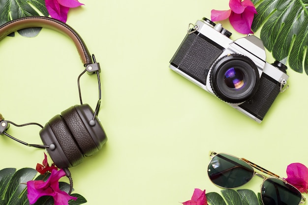 Superficie verde con cámara retro, auriculares y gafas con flores tropicales.