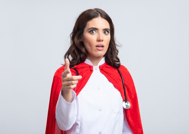 Supermujer ansiosa en uniforme médico con capa roja y puntos de estetoscopio en el frente aislado en la pared blanca