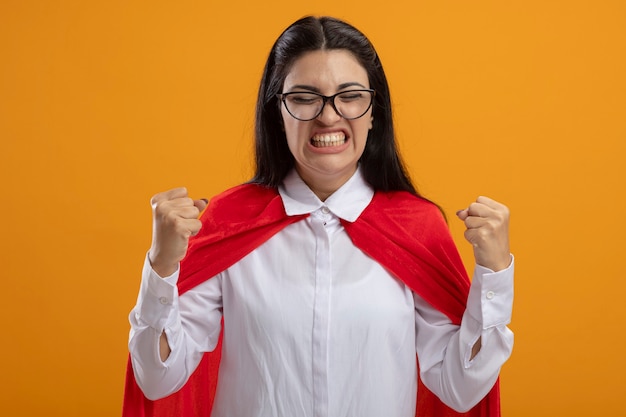 Foto gratuita superwoman joven alegre con gafas haciendo gesto de sí con los ojos cerrados aislados en la pared naranja