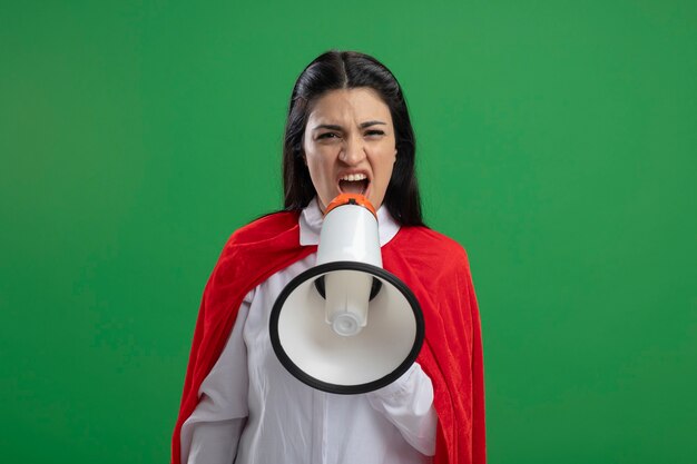 Superwoman joven gritando en altavoz mirando al frente aislado en el espacio de copia de pared verde