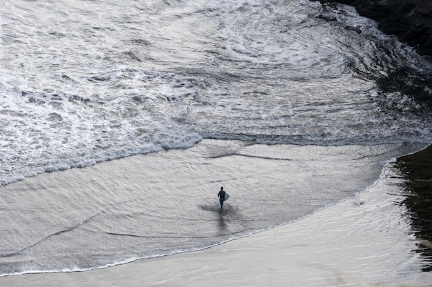 Surfer caminando hacia el mar mientras sostiene una tabla de surf en Nueva Zelanda