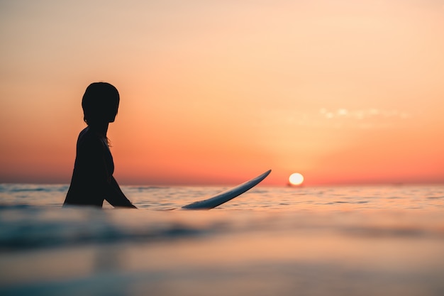 Foto gratuita surfer en el océano con la impresionante puesta de sol en el cielo de fondo