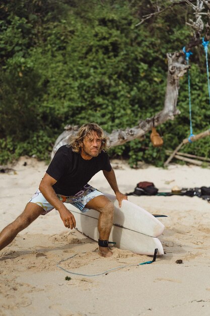 Un surfista de cabello blanco y rizado con una tabla de surf va a surfear.