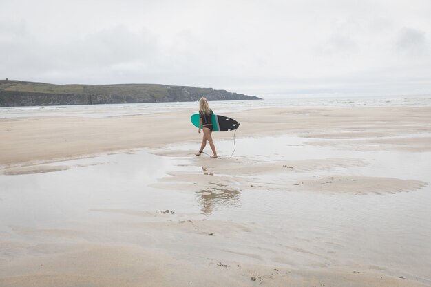 Surfista femenina caminando por una playa con tabla de surf