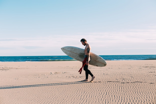 Surfista de moda hipster en la playa con tabla de surf