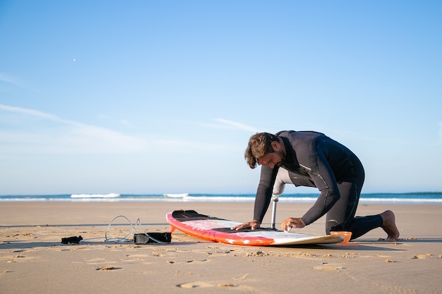 Surfista serio en traje de neopreno vistiendo una extremidad artificial, tabla de encerado en la arena de la playa