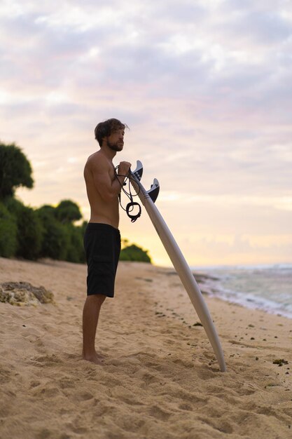 Surfista sexy surfista con tabla de surf. Un apuesto joven atleta sosteniendo una tabla de surf con el pelo mojado en unas vacaciones deportivas en la playa de verano. Destino de viajes deportivos. Estilo de vida de surf.