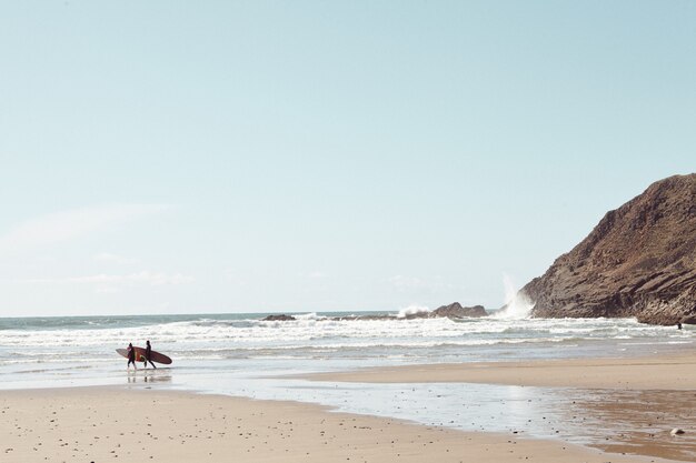 Surfistas en la distancia en la playa rocosa