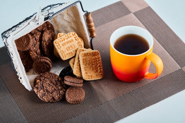 Surtido de galletas, dulces y una taza de té en superficie gris.